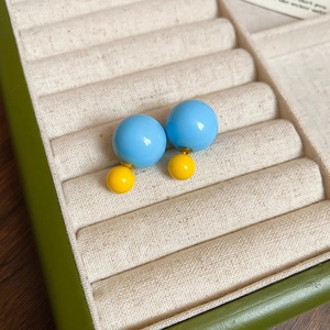 Detail of yellow and blue double-sided spherical stud earrings on beige velvet tray