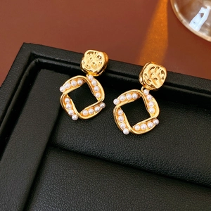 Macro shot of gold square earrings with white pearls on a black leather display