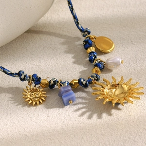 Macro shot of a braided cord necklace with 18K gold sun pendants and a white pearl