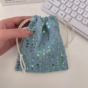 Close-up of a blue denim drawstring pouch featuring shimmering green sequin vertical stripes