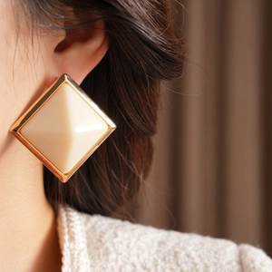 Close-up of diamond-shaped resin stud earring with gold-tone alloy frame on ear