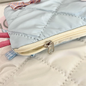 Close-up of a light blue quilted cosmetic bag featuring a bow and silver metal zipper