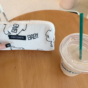 Close-up of white corduroy pencil case with embroidered black lines on a wooden table