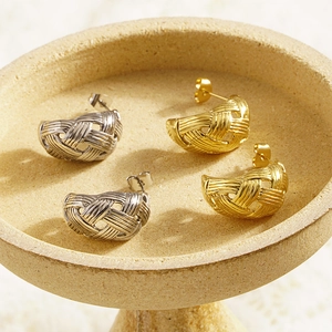 Hollow woven teardrop hoop earrings in gold and silver finish on ceramic tray