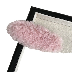 Pink plush oval hair clip with fuzzy texture on minimalist display stand for women