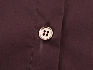 Macro detail of a chestnut woven shirt showing the gold-rimmed button and fabric texture