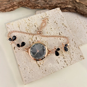 Macro shot of rose gold bracelet watch with black butterfly charms on a stone surface