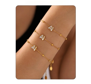 Macro shot of three 18k gold butterfly bracelets with white mother of pearl on a wrist