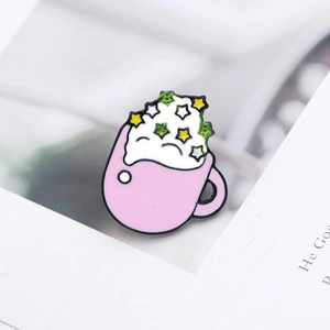 Macro shot of a pink coffee cup enamel pin with colorful star motifs on magazine pages