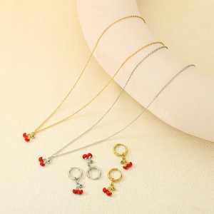 Detail of red cherry pendant jewelry set with gold and silver necklaces and hoop earrings