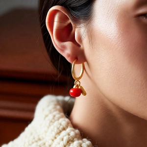 Close-up of golden hoop earring featuring a red berry bead and gold leaf on a female model