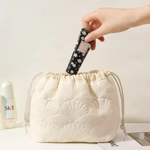 Detail view of white quilted drawstring bag being filled with hand cream and cosmetics