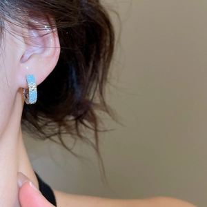 Side view of silver huggie hoop earrings with blue and clear zircon on model's ear