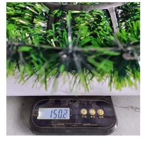 Detailed view of a green Christmas tinsel wreath being weighed, showing a weight of 150.2g