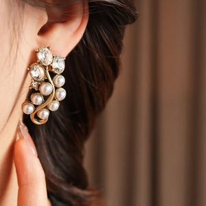 Close-up of vintage gold earring with oval rhinestones and white pearls on a model