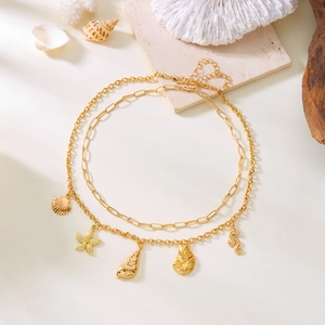Detail of gold double-layer necklace with starfish, shell, and seahorse charms on coral