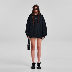 Vue de face d'un sweat à capuche noir oversize avec logo croix blanche sur la poitrine