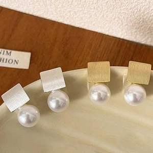 Gros plan détaillé de boucles d'oreilles carrées en métal avec perles blanches en or et argent