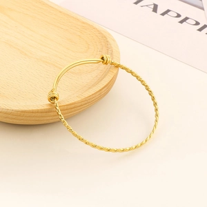 Detail of adjustable gold twist bangle featuring a dual-texture design on a wooden tray