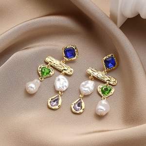 Detail of baroque pearl drop earrings with colorful gemstones on gold satin fabric