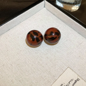 Macro detail of glossy leopard print resin ball earrings on a jewelry display box