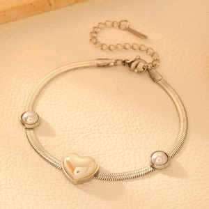 Détail du bracelet chaîne serpent dorée avec perles blanches et breloque cœur irisant