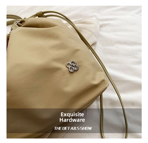 Detailed close-up of a silver four-leaf clover metal logo on a beige nylon tote bag
