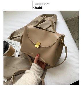 Close-up of khaki leather handbag with gold square buckle on a stylish bed setting