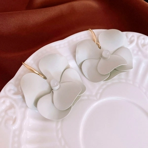 Detailed macro of matte white flower earrings with gold hooks on a ceramic dish