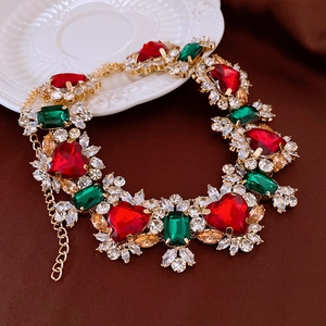 Detail of vintage gold necklace with large red heart gem and green crystal accents
