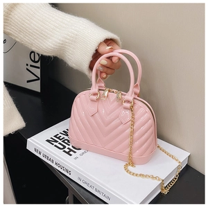 Detailed close-up of pink jelly shell bag with gold zippers and chain strap on books