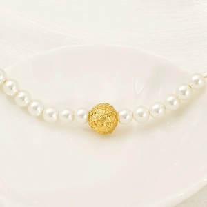 Collier ras du cou en perles avec breloque dorée ajourée sur un plateau en coquillage