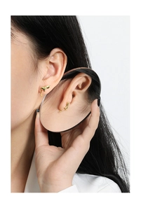 Macro shot of gold liquid lava stud earrings on model reflecting in a round hand mirror