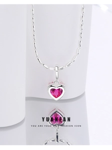 Detail shot of heart pendant necklace with pink gemstone and silver bead chain on white base