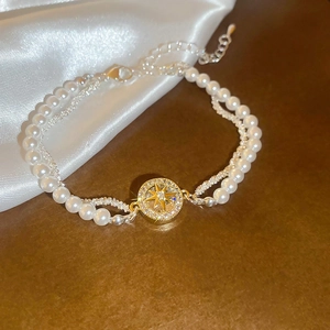 Detail eines zweilagigen Perlenarmbands mit goldenem Sternanhänger und Zirkonia-Steinen