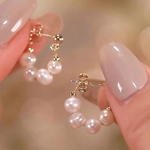 Macro shot of elegant round pearl earrings in a gold circular layout held by a hand