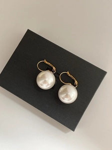 Detailed close-up of white resin pearls on gold plated leverback earrings on black box