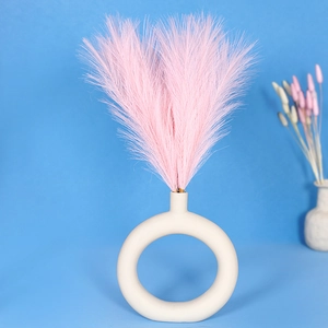 Artificial pink pampas grass bouquet in a white ceramic ring vase against blue background
