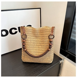 Detail view of a woven straw bag featuring a unique brown wooden bead handle on a black surface