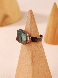 Vista macro di anello in rame vintage con fluorite verde grezza su supporto in legno