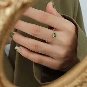 Detail of adjustable gold chain ring with emerald cut green zircon on finger