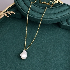 Elegant irregular baroque pearl necklace with golden chain on green velvet stand