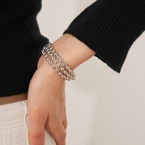 Dettaglio di un bracciale a tre strati con perle d'argento indossato su sfondo minimalista