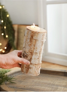 Close-up of a natural birch wood candle holder with rustic bark and a burning white candle