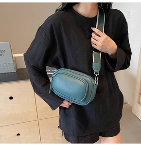 Deep teal textured crossbody bag with dual zippers and wide woven strap on a model