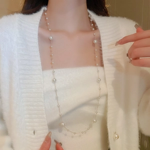 Detailed view of long gold-plated necklace with irregular white pearls on a model