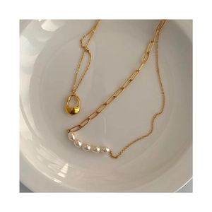 Elegant gold chain necklace with white pearls and drop pendant on ceramic tray