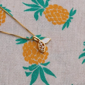 Detailed close-up of a golden mermaid tail necklace with white enamel and clear zircons