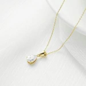 Elegante collar dorado con colgante de gota sobre tela blanca y cerámica