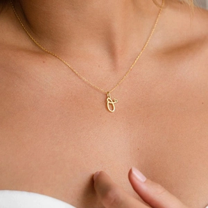 Close-up of a gold-plated letter O pendant necklace with a tiny heart on the collarbone